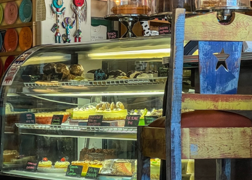 A display case filled with various desserts, including cakes and pastries, next to a colorful wooden chair.