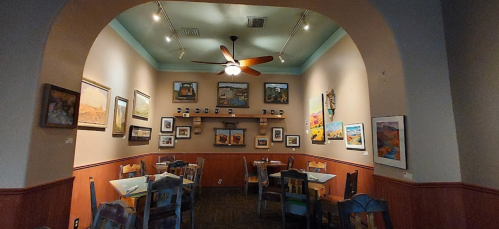 Cozy restaurant interior with wooden tables, chairs, and colorful artwork on the walls under soft lighting.