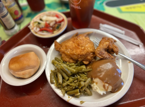 A plate with fried chicken, green beans, mashed potatoes with gravy, a roll, and a side salad, with a drink nearby.