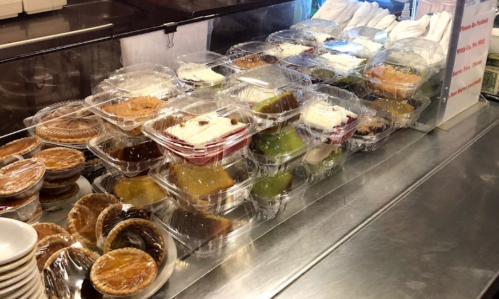 A display of assorted desserts in clear containers, including pies and cakes, arranged on a counter.
