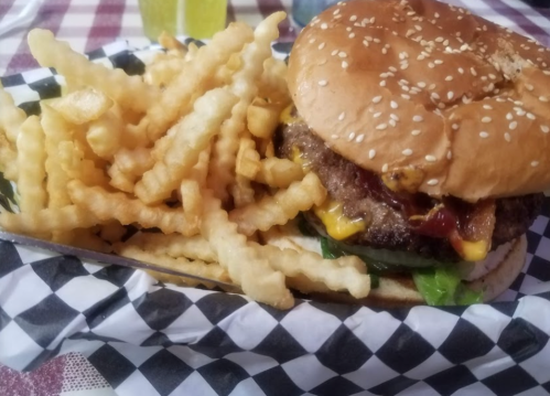 A sesame seed bun burger with cheese, lettuce, and condiments, served with a side of crinkle-cut fries.