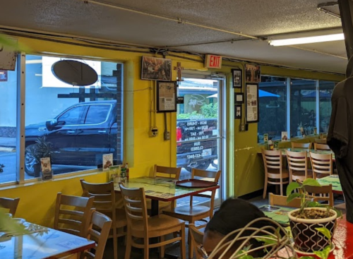 Interior of a restaurant with yellow walls, wooden tables, and a view of a parked car outside through large windows.