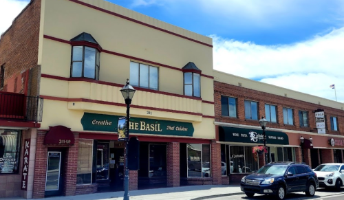 A street view of a building featuring "The Basil" restaurant and various shops, with a blue sky above.