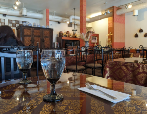 A cozy restaurant interior with empty tables, decorative walls, and two water glasses on a patterned table.