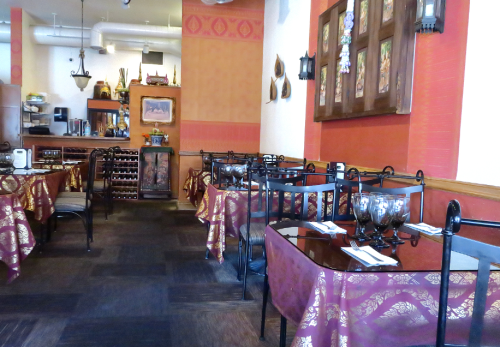 Interior of a restaurant with red walls, elegant tables covered in patterned cloth, and decorative wall art.