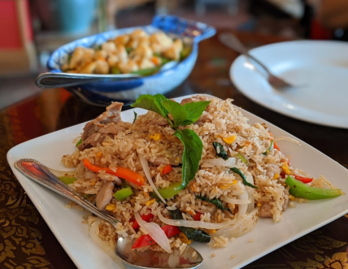 A plate of fried rice with vegetables and meat, garnished with basil, next to a bowl of stir-fried vegetables.