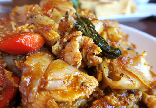 A close-up of a flavorful chicken stir-fry with vegetables and spices, served in a white bowl.
