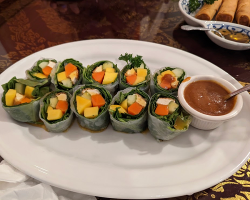 A plate of fresh spring rolls filled with vegetables and mango, served with a small bowl of dipping sauce.