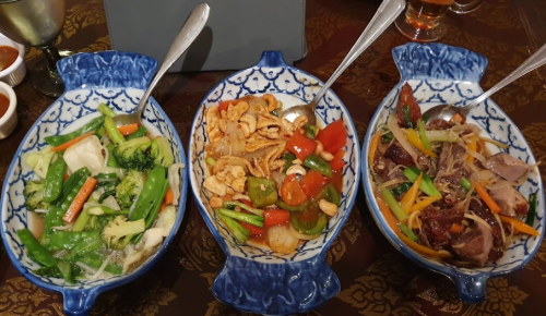Three colorful dishes in blue patterned bowls: mixed vegetables, chicken with peppers, and a meat stir-fry with noodles.