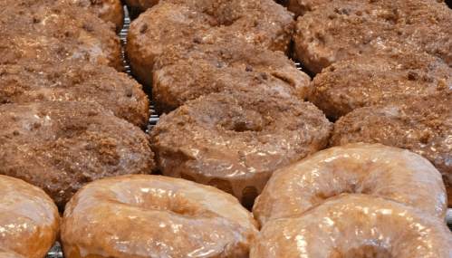 A close-up of assorted donuts, including glazed and crumb-topped varieties, arranged on a cooling rack.