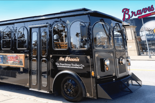 A black trolley bus parked near a stadium, featuring signage for the Peachtree Trolley Company.