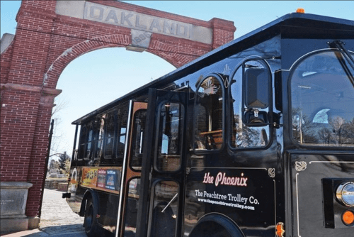 A black trolley bus parked under an archway labeled "Oakland," with trees in the background.