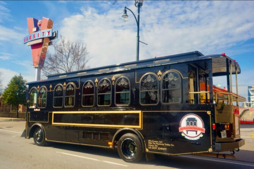 A vintage-style black trolley bus parked near a retro sign for "The Varsity" restaurant on a sunny day.