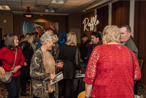 A lively gathering of people at a raffle event, with attendees chatting and enjoying drinks in a decorated room.