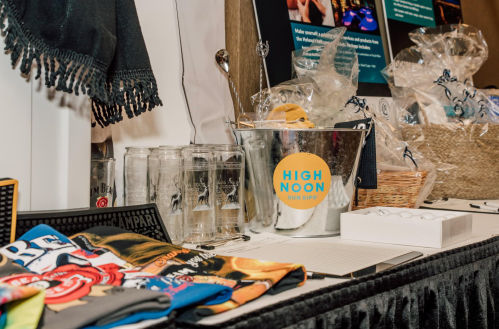 A table display featuring a bucket of drinks, glasses, and promotional items, including colorful shirts and a basket.