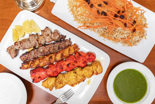 A platter of assorted grilled kebabs with lemon slices, served alongside a plate of rice with carrots and raisins.