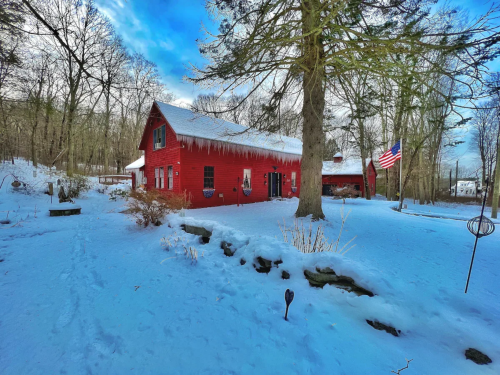 A red house surrounded by snow, with icicles hanging from the roof and trees in the background. An American flag is visible.