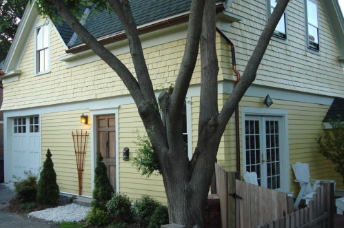 A yellow house with a tree in front, featuring a garage, porch, and landscaped yard.