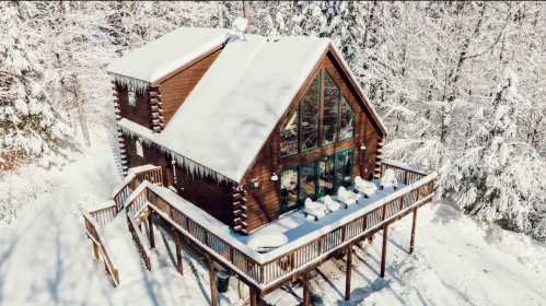 A cozy wooden cabin with a large deck, surrounded by snow-covered trees in a winter landscape.