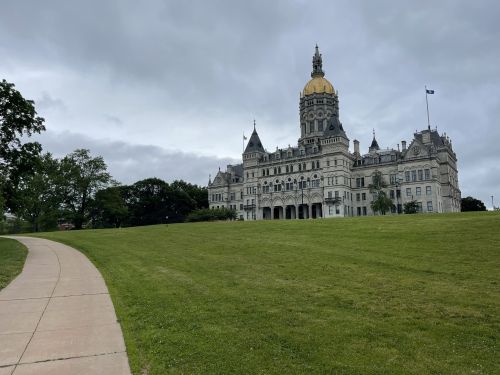 A grand building with a golden dome, surrounded by green grass and trees, under a cloudy sky.