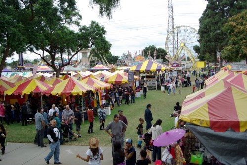 A vibrant fair scene with colorful tents, a ferris wheel, and crowds enjoying various attractions and activities.