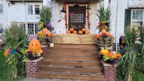 A decorated porch with pumpkins, hay bales, and colorful autumn flowers, creating a festive fall atmosphere.