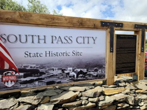 Sign for South Pass City State Historic Site, featuring a wooden frame and a backdrop of historical images.
