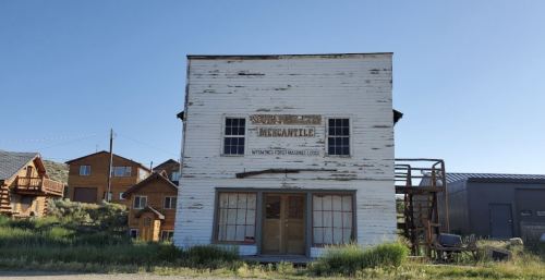 Old wooden building with a faded sign reading "Mercantile," surrounded by grass and other rustic structures.