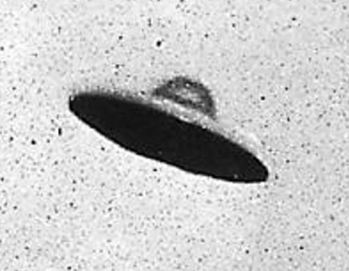 A black and white image of a classic flying saucer-shaped UFO against a speckled background.