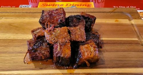 A wooden platter with a stack of crispy, caramelized beef cubes, glistening with sauce.
