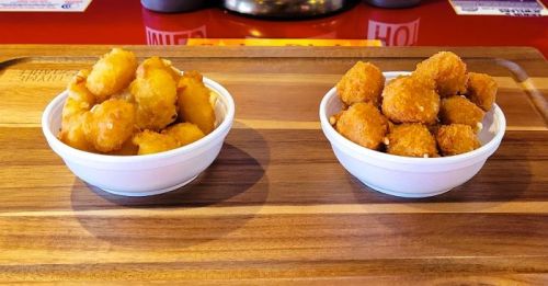 Two white bowls on a wooden tray, one filled with golden tater tots and the other with crispy cheese balls.