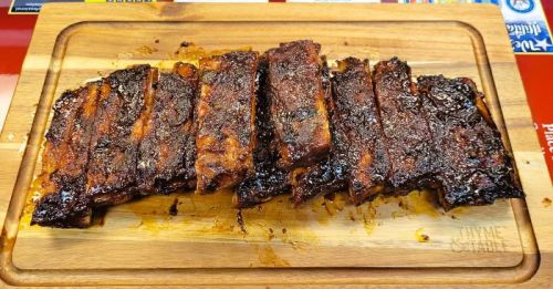 Sliced, charred ribs arranged on a wooden cutting board, glistening with sauce.