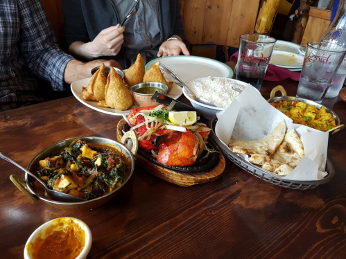 A table spread with various Indian dishes, including samosas, rice, curry, grilled chicken, and naan.