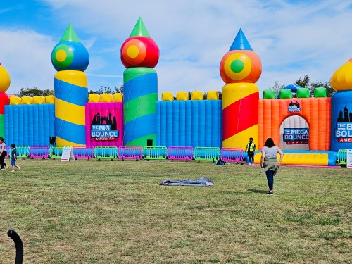 Colorful inflatable bounce house with towers, set in a grassy area, with people enjoying the attraction.