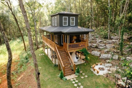 A modern treehouse surrounded by trees, featuring a wooden deck, stairs, and a cozy outdoor seating area.