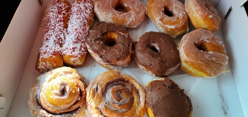 A box of assorted donuts, including glazed, chocolate-covered, and coconut-topped varieties.
