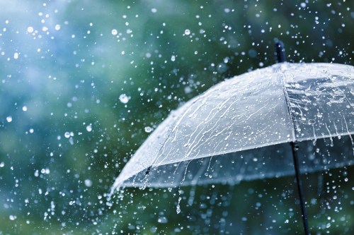 A close-up of a transparent umbrella surrounded by falling rain, with droplets splashing against its surface.