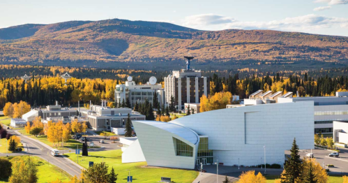 A modern building in the foreground with a backdrop of colorful autumn trees and mountains under a clear blue sky.