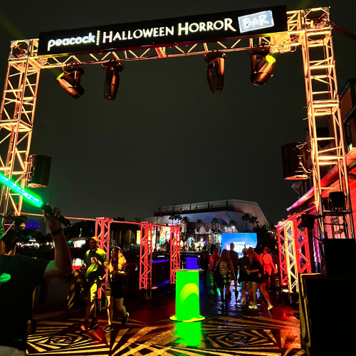 Entrance to Peacock's Halloween Horror Bar, featuring colorful lights and a festive atmosphere on a rainy night.