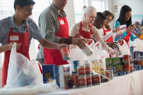 A diverse group of volunteers in red aprons sorting food items at a community service event.