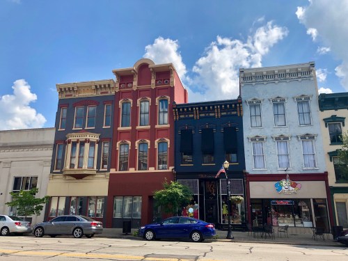 Historic downtown buildings with colorful facades under a blue sky, featuring shops and parked cars.