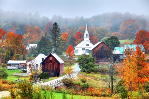 A scenic autumn landscape featuring a church, barns, and colorful trees in a misty rural setting.