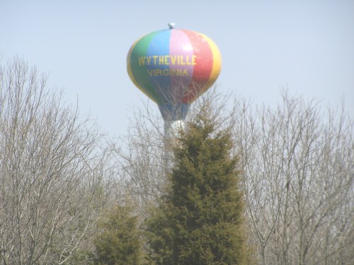 A colorful hot air balloon with "Wytheville Virginia" written on it, rising above bare trees against a clear sky.