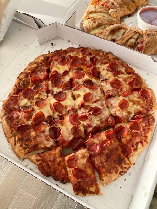 A pepperoni pizza with melted cheese, partially sliced, in a pizza box on a light-colored surface.