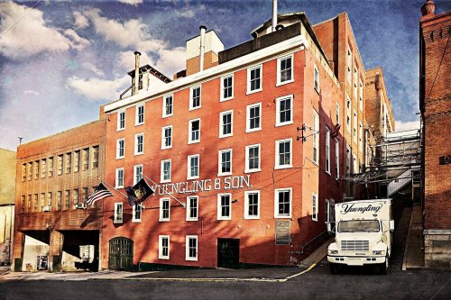 Historic brick brewery building with "Yuengling & Son" sign, American flag, and delivery truck parked outside.