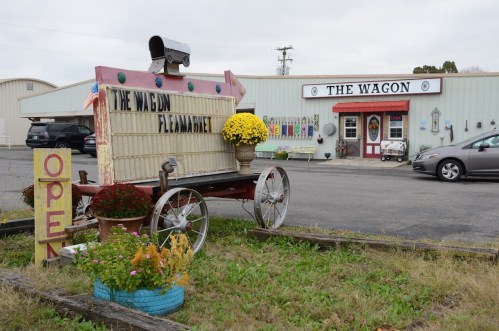 A colorful sign for "The Wagon Flea Market" outside a shop, with flowers and a vintage cart in the foreground.
