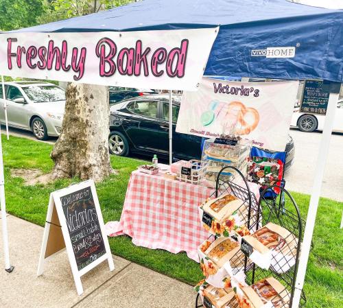 A market stall with a blue canopy, featuring a "Freshly Baked" sign, baked goods, and a checkered tablecloth.