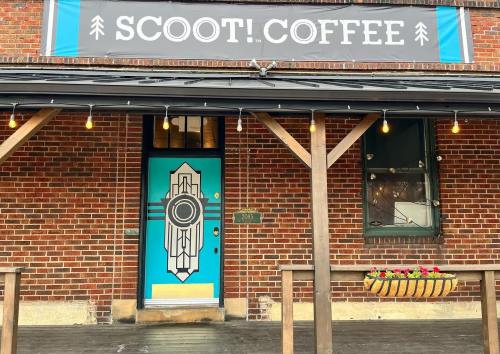A bright turquoise door with a geometric design, under a sign that reads "SCOOT! COFFEE," on a brick building.