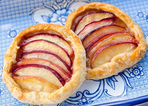 Two fruit tarts with sliced apples and plums on a blue decorative plate.