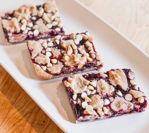 Three dessert bars with a berry filling, topped with cookie crumbles and white chocolate chips, on a white platter.
